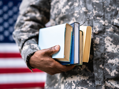 Closeup of army officer students' hands holding small stacks of books against the American flag backdrop.
