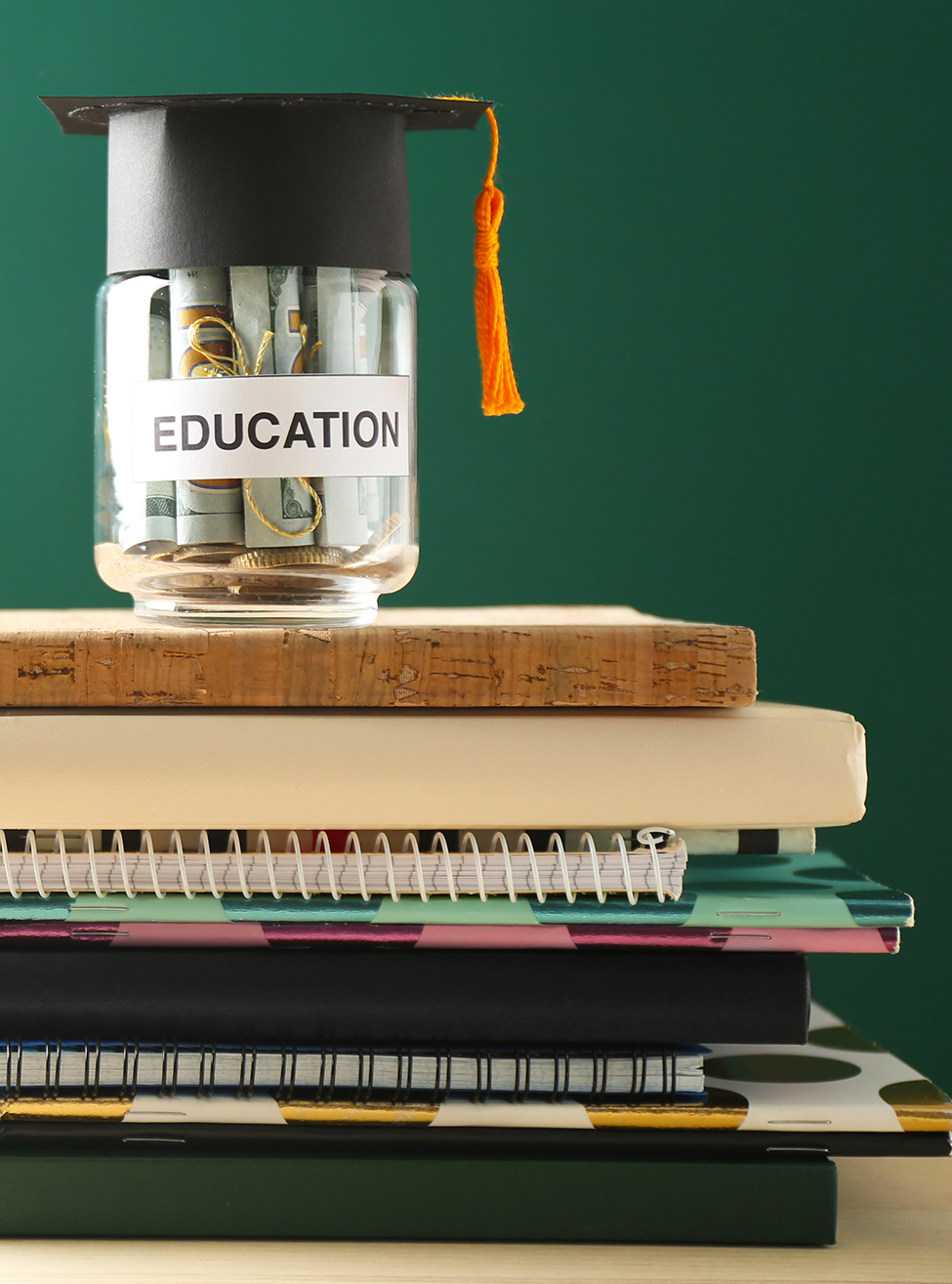 School supplies and glass jar with money for education on wooden table against green background