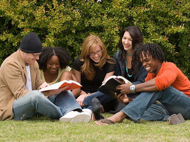 group of adults of varying ages sitting in the grass reading books