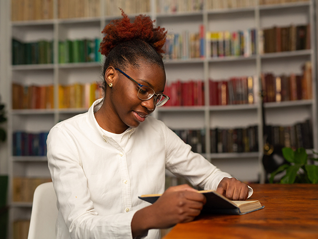 young female student reading a book at a table in the library