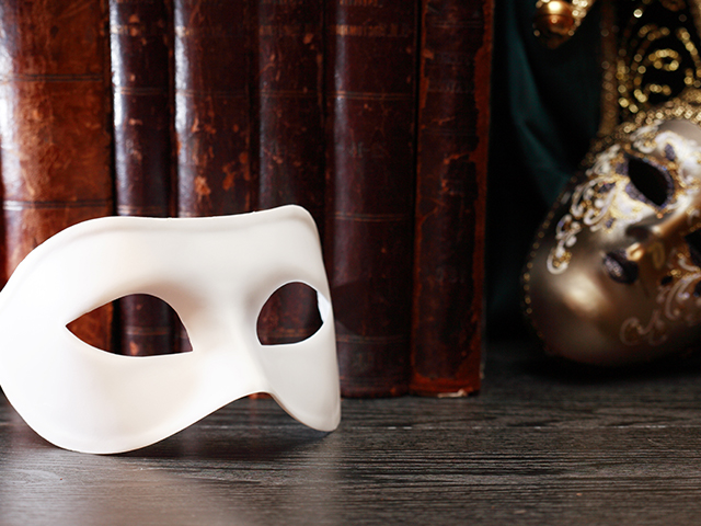 Theater concept. Closeup of white classical simple masquerade mask infront of books