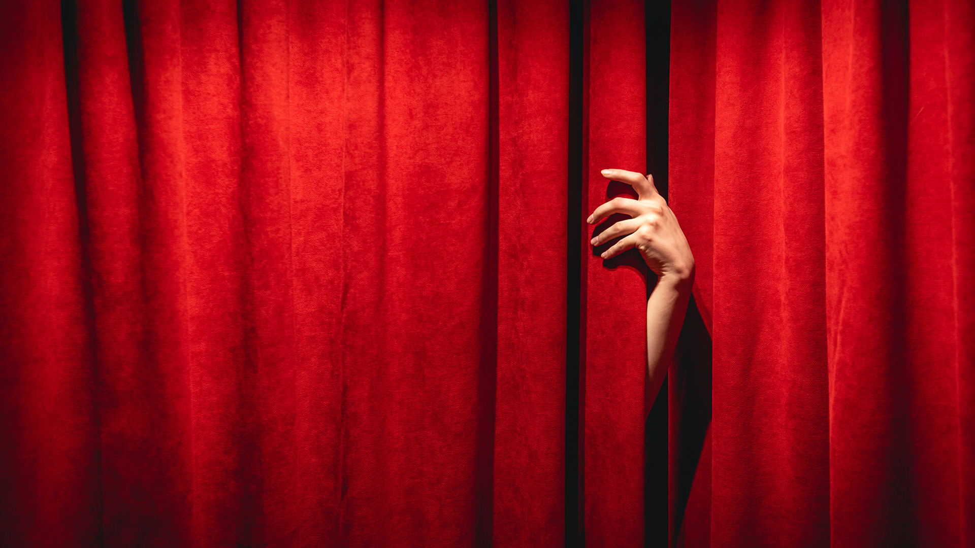 hand peeking through the middle of red theatre curtain