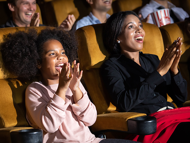 Happy African-American woman and young girl watching profuction in theatre