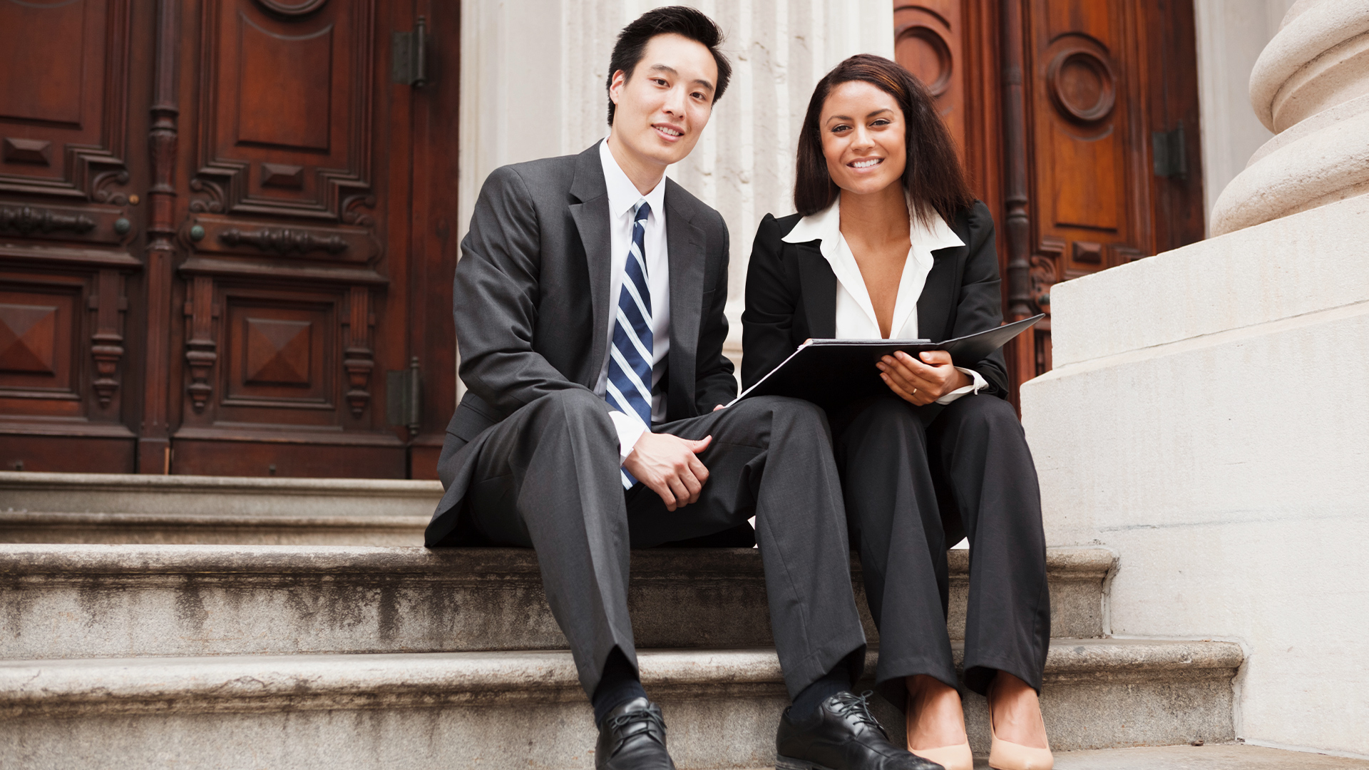Businessman and business woman smiling and sitting outside on steps of legal building