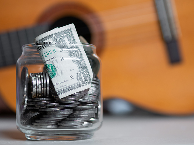 Money in glass jar in front of a guitar