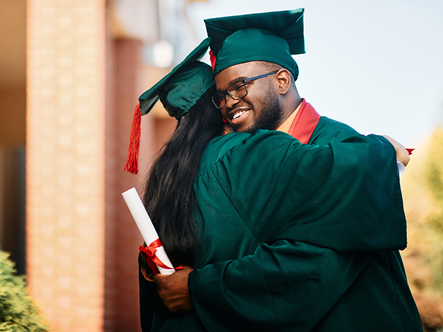 Happy black college student and his female friend hug each other while celebrating their graduation