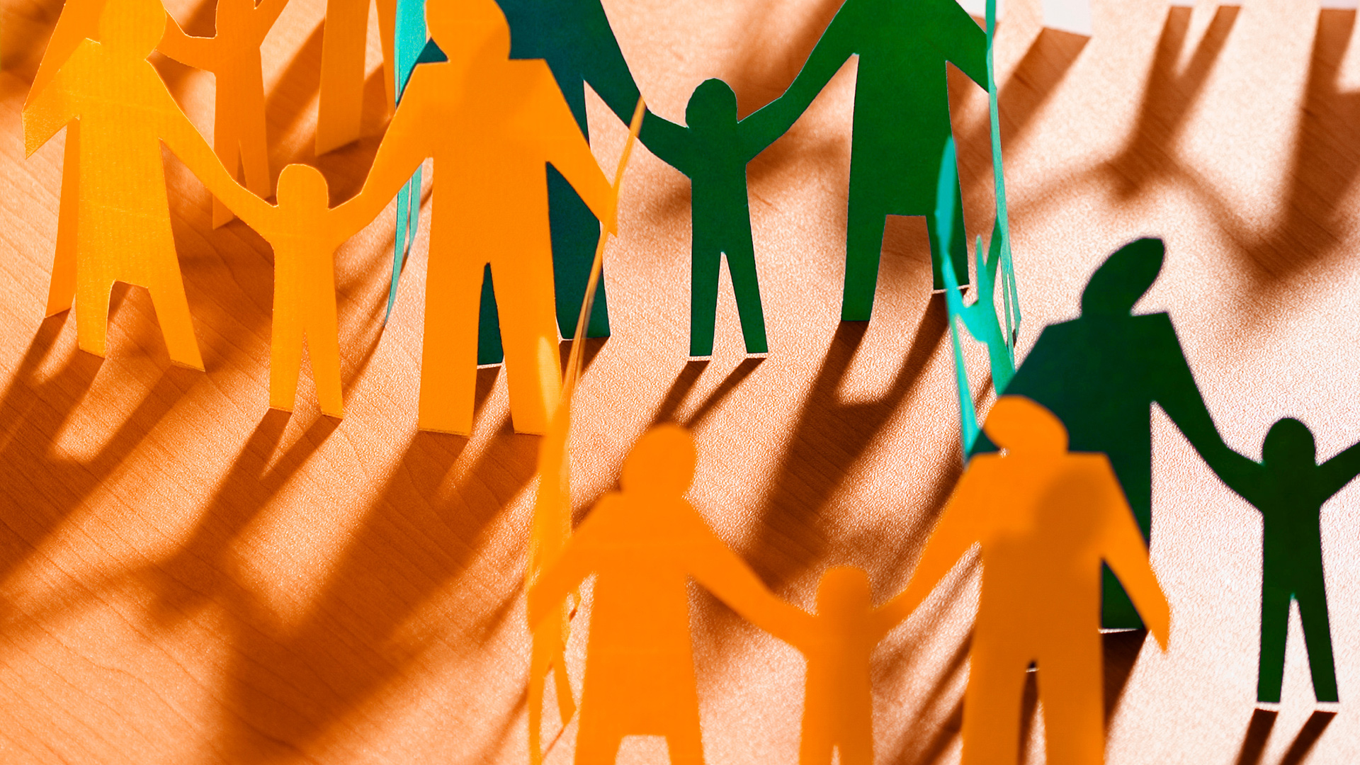 orange and green paper cutout people satnding on wood table