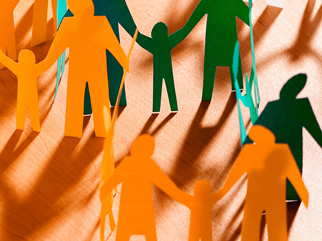 orange and green paper cutout people satnding on wood table