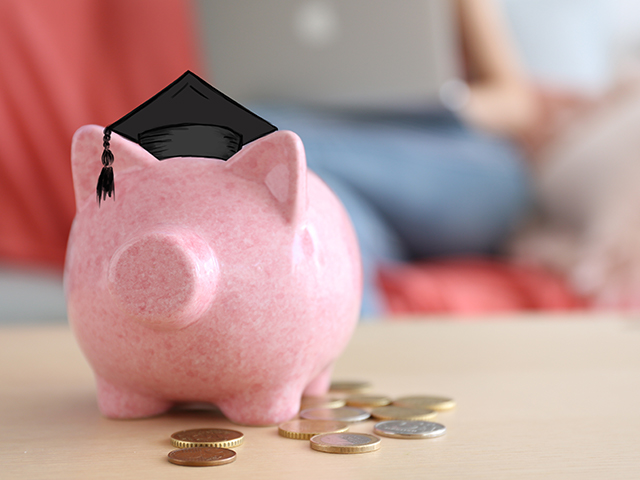 Pink piggy bank with graduation cap and coins sitting on wood table