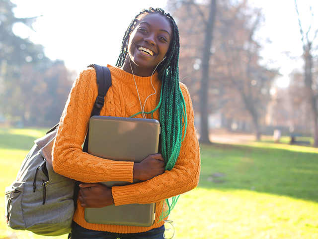 Female student with green braids smiling holding laptop