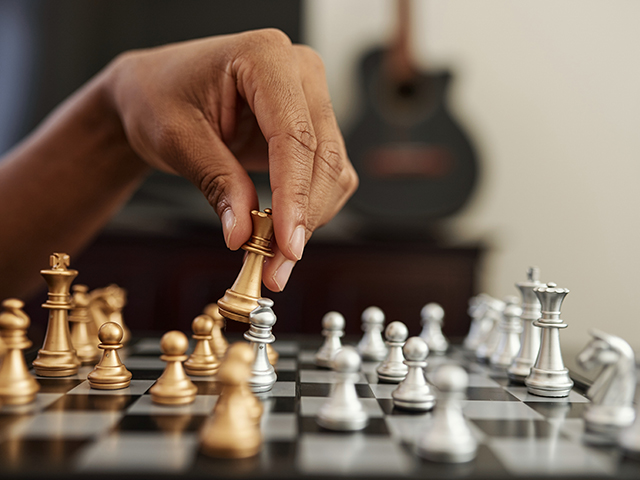 A close-up of a hand strategically moving a gold chess piece on a chessboard