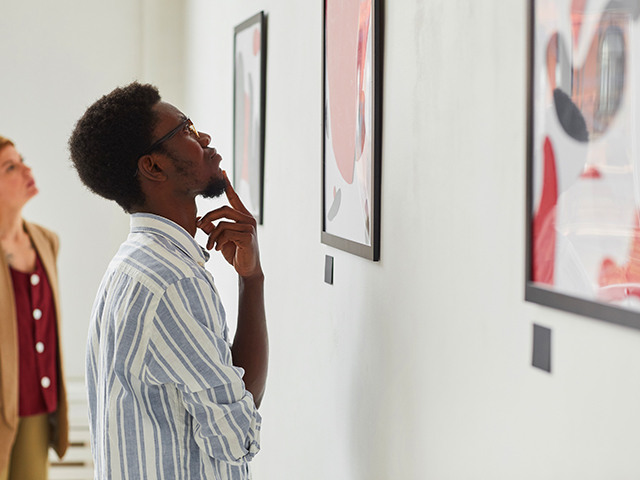 Side view portrait of young African-American man looking at paintings while exploring modern art gallery exhibition