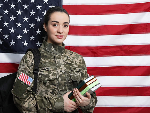 A young female military member holding books in front of an American flag.